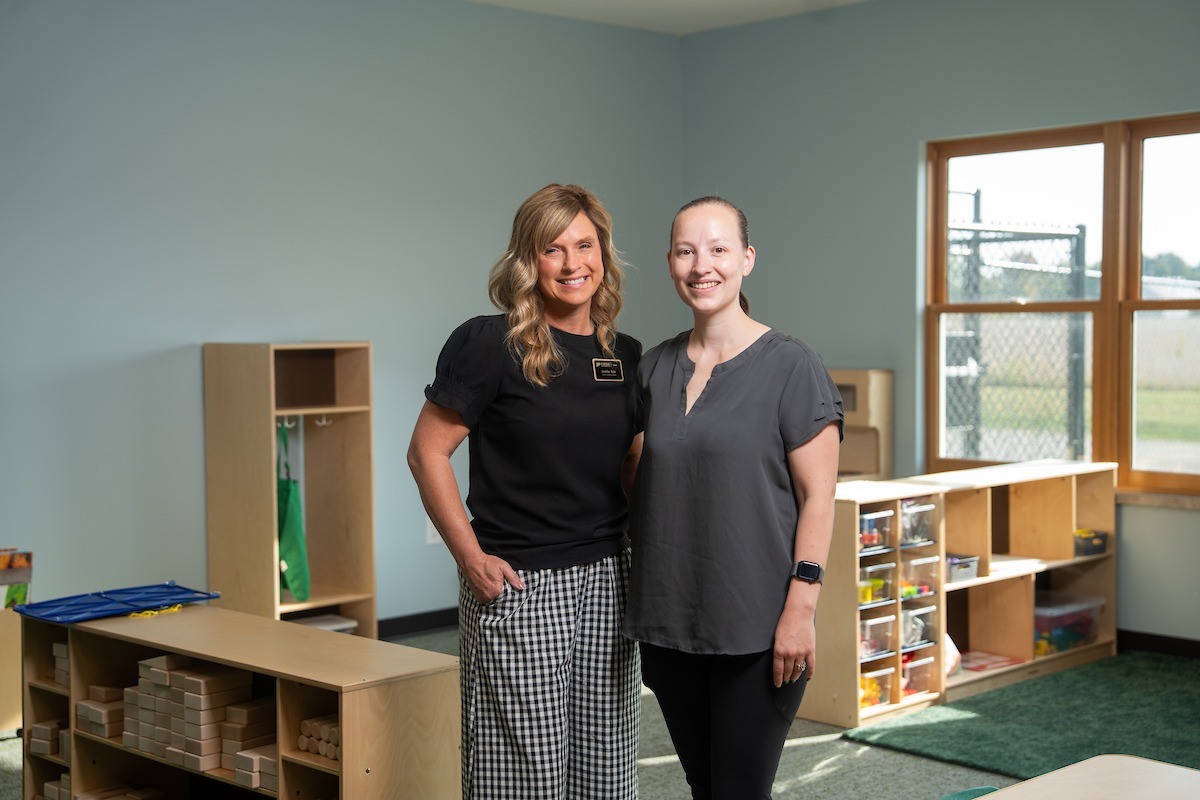 Two women standing inwards with one another smiling in a classroom.