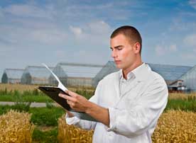 Image of a man looking at a clipboard with a field in the background.