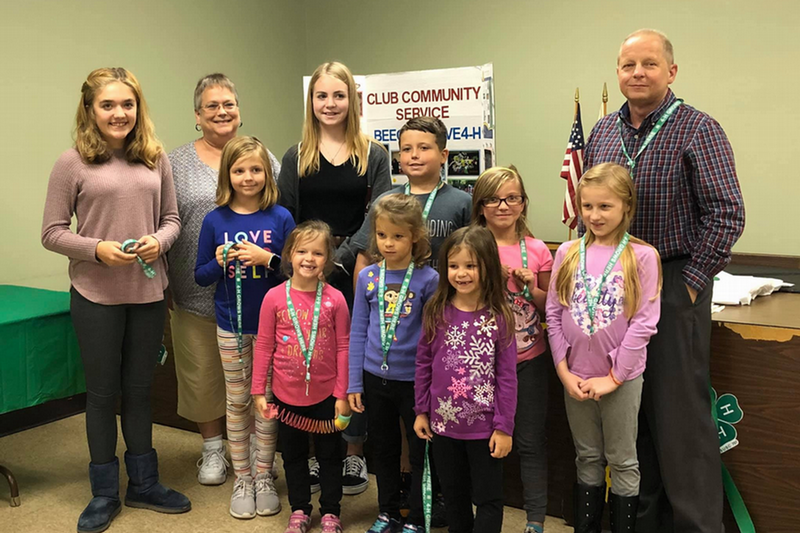 group of 4-H youth and adult smiling in front of a Community Service poster
