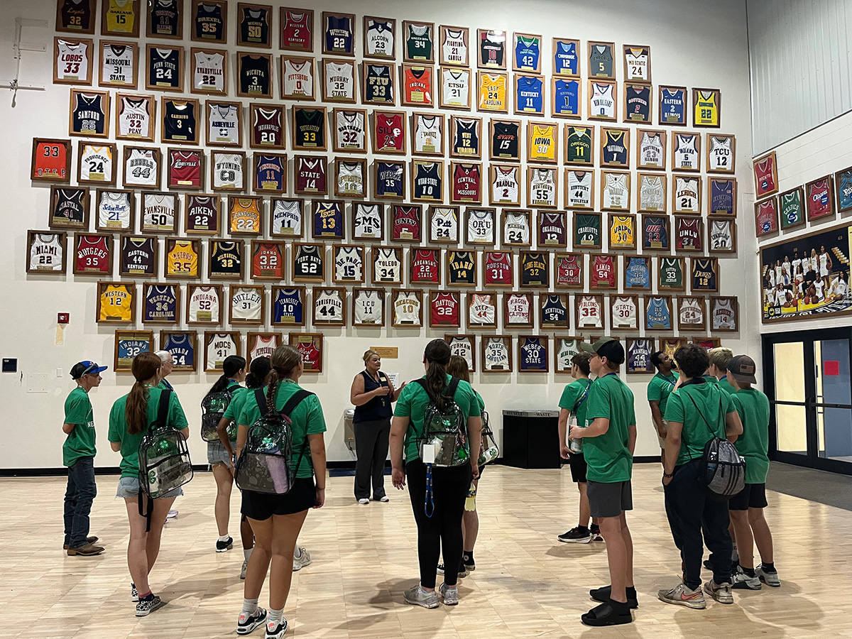 GROUP OF 4-H YOUTH STANDING IN A CROWD AND LOOKING AT WALL OF JERSEYS