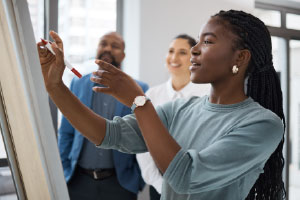 Woman Writing on Whiteboard while talking to two men