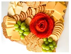 salami rose surrounded by crackers and cheese slices with green grapes 