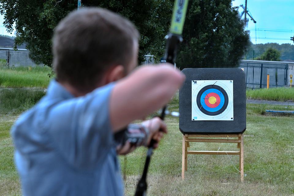 boy aiming bow and arrow at target board