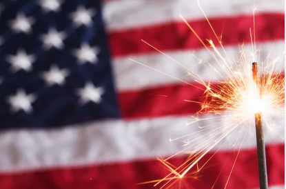 US flag with lit sparkler in front of it.