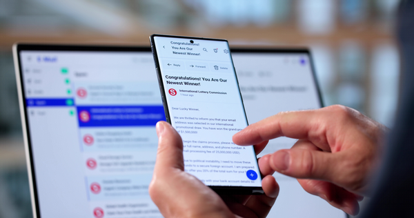 Photo of hand hold cell phone and a laptop computer screen in the background