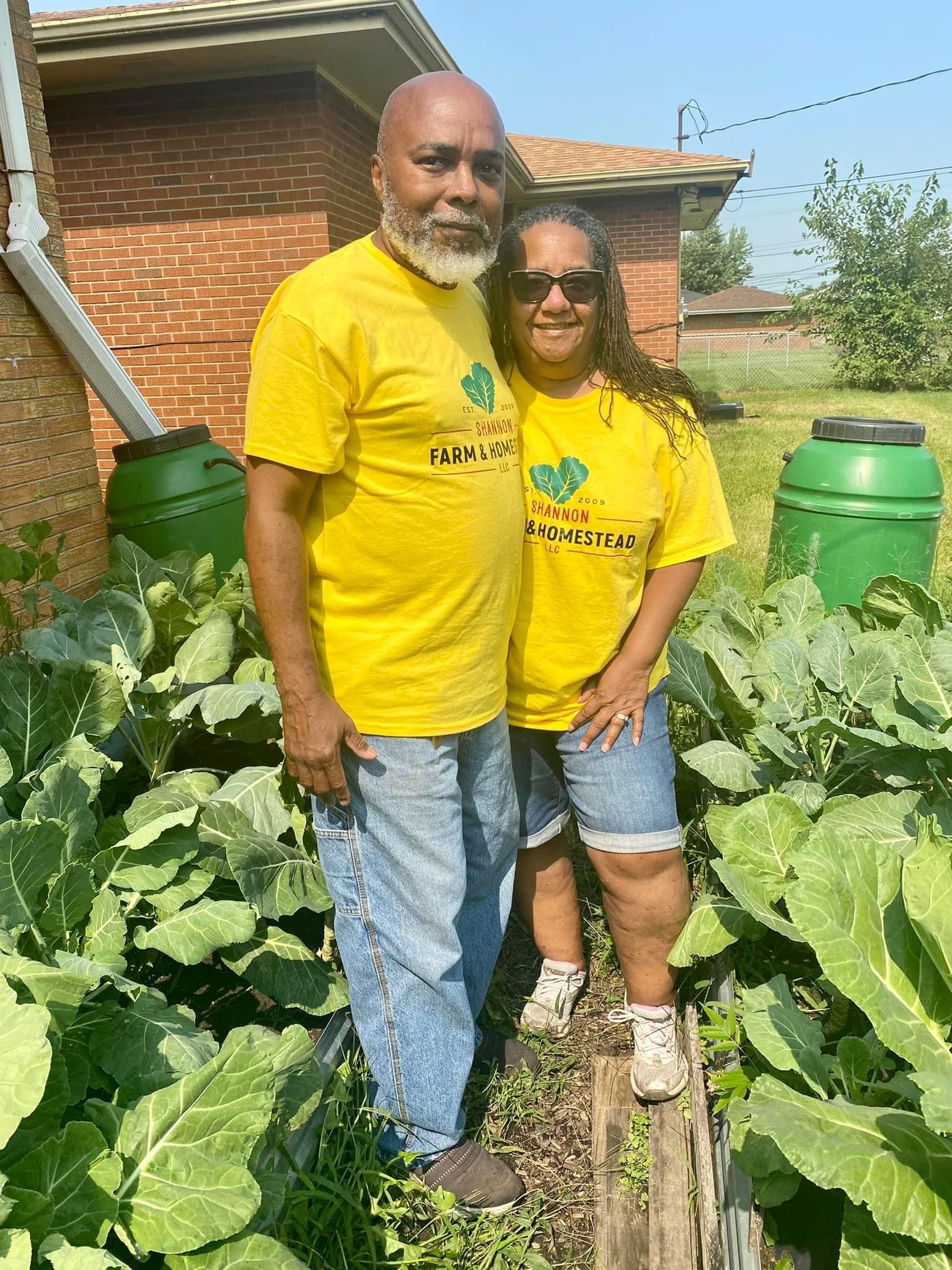 Man and woman stand with yellow shirts in front of raised garden beds.