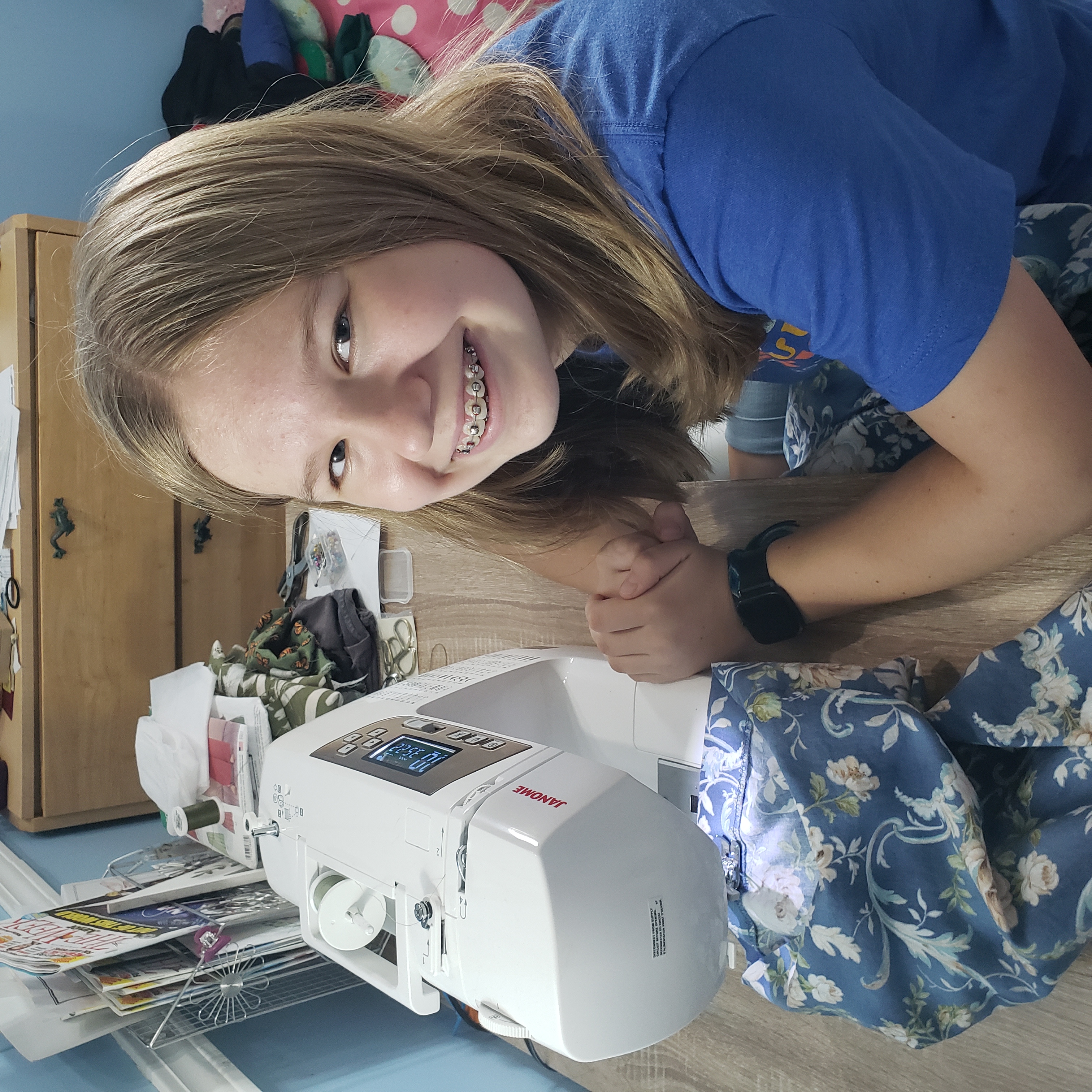 4-H youth grins at camera while sewing a green dress.