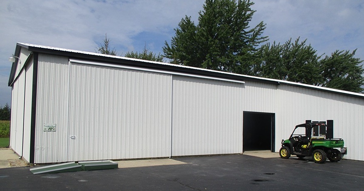 A vehicle sits outside of a farm shop, a long building with metal siding.