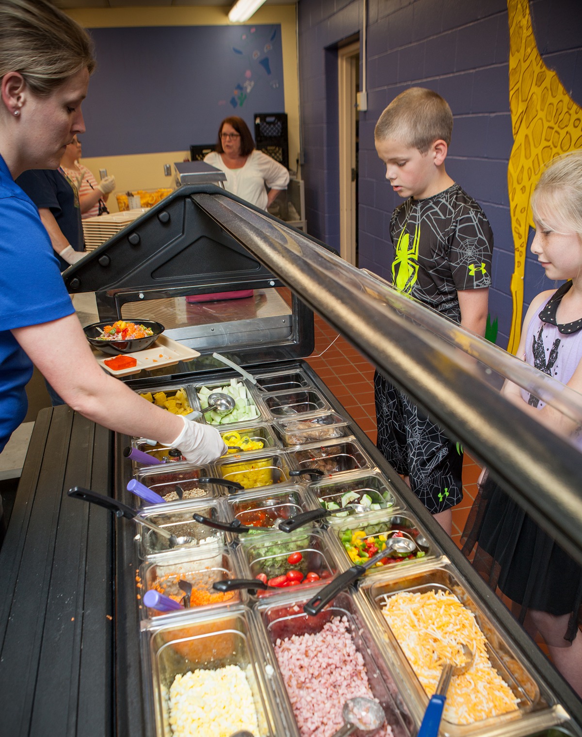 A lunch server creates a salad for a student