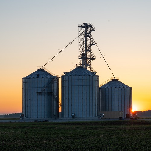 Three grain bins standing with the sun behind them.