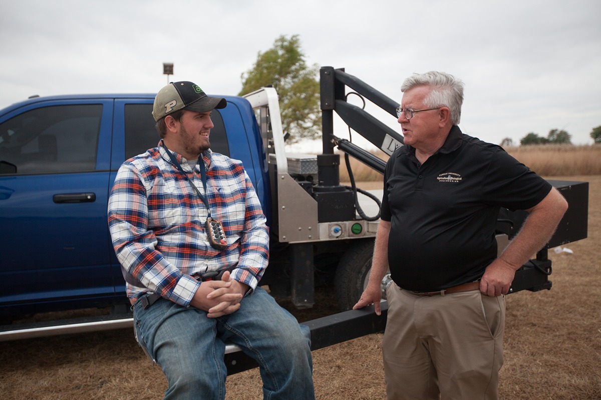  A farmer, seated in a truck-mounted lift, talks to AgrAbility staff member Bill Fields