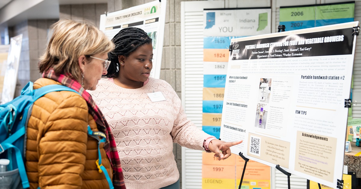 A Purdue student shows her research poster to a conference attendee