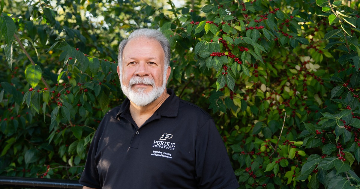 Lenny Farlee smiling in front of an invasive honeysuckle bush.
