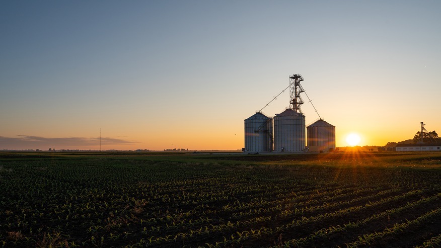 The sun rises behind three grain bins.