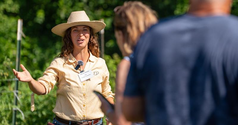 A woman gestures to a field of plants.