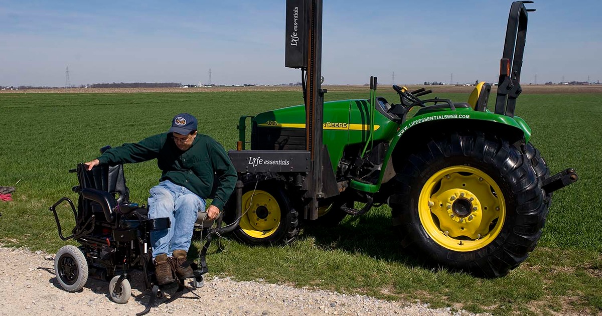 A man transfers from an assistive seat lift on a tractor into a wheelchair 