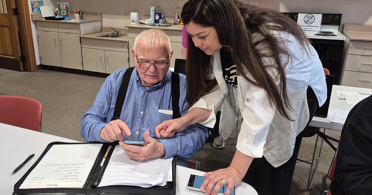 A man, left, holds a smart phone while a woman, right, looks at the man’s phone and gestures to the screen